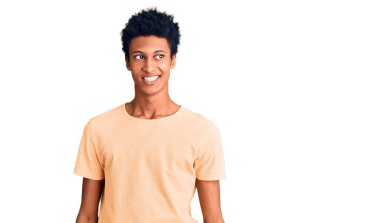 Genç Afro-Amerikan bir adam günlük kıyafetler giyip yüzünde gülümseme, doğal bir ifade ile yan yana bakıyor. Kendinden emin gülen. 