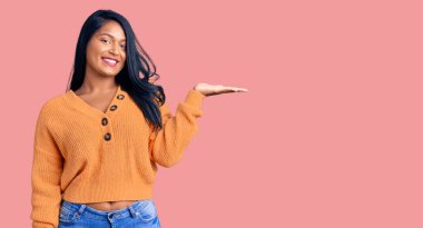 Uzun saçlı, sıradan bir kazak giyen, neşeli bir şekilde gülümseyen ve avuç içi kameraya bakan İspanyol bir kadın.. 