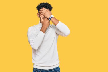 Gündelik kazak giyen genç Arap adam gözlerini ve ağzını elleriyle kapatıyor, şaşırmış ve şok olmuş. duygu gizleme 