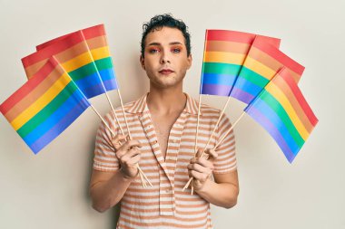 Elinde gökkuşağı lgbtq bayrakları tutan yakışıklı bir adam yüzünde ciddi bir ifadeyle rahatlamış. Basit ve doğal bir şekilde kameraya bakıyorsun.. 
