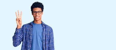 Genç Afro-Amerikalı günlük kıyafetler ve gözlük takmış üç numaralı parmaklarıyla onu gösterirken kendinden emin ve mutlu bir şekilde gülümsüyor.. 