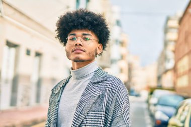 Genç Afro-Amerikan iş adamı ciddi bir ifadeyle şehirde duruyor..