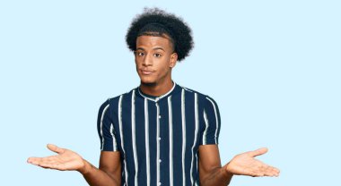 Afro saçlı, sıradan kıyafetler giyen, elleri ve kolları havada, kafası karışmış Afro-Amerikan bir adam. şüphe kavramı. 