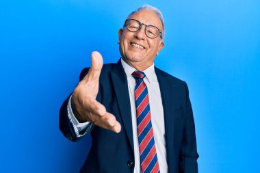 İş elbisesi giyen ve kravat takan beyaz bir adam selamlama ve hoş geldin demek için gülümseyerek tokalaşıyor. başarılı iş. 