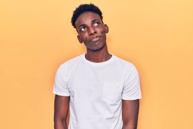 Genç Afro-Amerikan adam günlük kıyafetler giyiyor gülümsüyor yan tarafa bakıyor ve düşünüyor. 