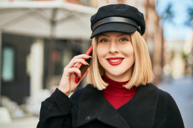 Genç sarışın kadın gülümsüyor. Şehirdeki akıllı telefondan konuşuyor..