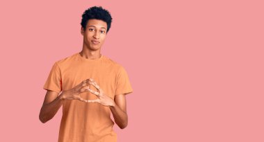 Genç, Afro-Amerikan bir adam günlük giysiler içinde ellerini birleştirip gülümseyerek rahat ve neşeli bir şekilde gülümsedi. Başarı ve iyimserlik 