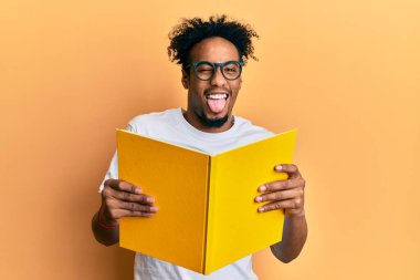 Genç Afro-Amerikalı sakallı adam kitap okuyor gözlüklü, dilini dışarı çıkaran komik bir ifade takınıyor.. 