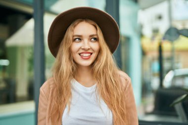 Genç sarışın kız gülümsüyor, mutlu bir şekilde şehirde duruyor..