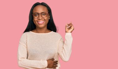 Gündelik kıyafetler ve gözlük takan genç siyahi kadın mutlu bir şekilde gülümsüyor. 