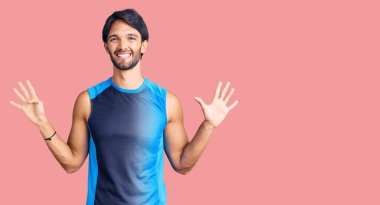 Yakışıklı, İspanyol giyinen, spor giyinen, dokuz numaralı parmaklarıyla işaret eden, kendinden emin ve mutlu gülümseyen adam.. 