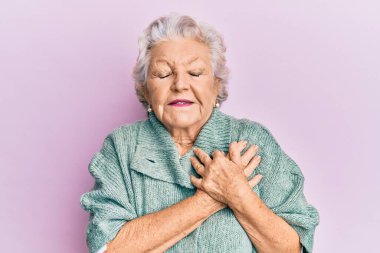 Yaşlı, gri saçlı, sıradan kıyafetler giyen, elleri göğsünde gülümseyen, gözleri kapalı, yüzünde minnet ifadesi olan bir kadın. sağlık kavramı. 