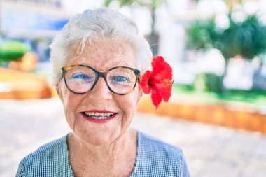 Yaşlı yaşlı, gri saçlı, dışarıda mutlu gülümseyen, dekoratif bir çiçek takan yaşlı kadın.