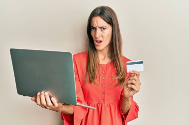 Genç ve güzel bir kadın dizüstü bilgisayar ve kredi kartını şok suratında tutuyor. Şüpheci ve alaycı görünüyor. Ağzını açtığında şaşırıyor. 