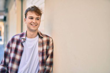 Genç beyaz adam gülümseyerek şehirde mutlu mesut duruyor..