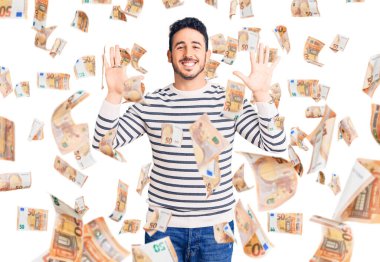 Gündelik kıyafetler giyen genç İspanyol adam on numarayı gösterip işaret ederken kendinden emin ve mutlu bir şekilde gülümsüyor..