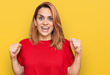 Latin kökenli genç bir kadın gündelik kırmızı tişört giyip kollarını kaldırıp, gözleri açık bir şekilde başarıyı kutluyor. Kazanan konsept. 