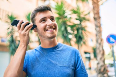 Kafkasyalı genç adam gülümsüyor. Şehirdeki akıllı telefonu kullanarak mutlu bir şekilde sesli mesaj dinliyor..