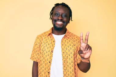 Saçları örgülü genç Afro-Amerikalı adam iki numarayı gösterip gösterirken kendinden emin ve mutlu bir şekilde gülümsüyor.. 