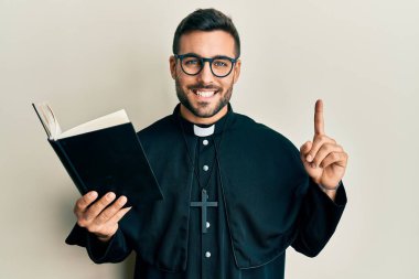 Genç İspanyol rahip elinde İncil 'le mutlu ve havalı bir gülümsemeyle gülümsüyor. diş gösterme. 