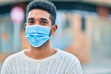 Sağlık maskesi takmış genç Afro-Amerikan adam şehirde dikiliyor..