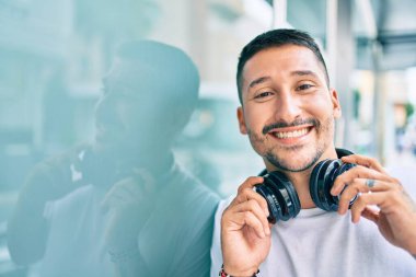 Genç İspanyol adam gülümsüyor. Mutlu bir şekilde müzik dinliyor. Şehir caddesinde kulaklık kullanıyor..