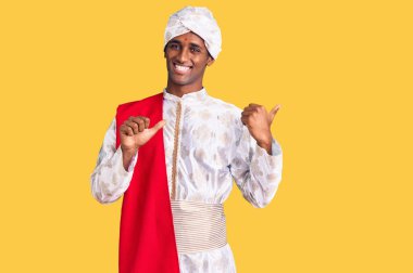 Geleneksel giyinmiş Afrikalı yakışıklı bir adam Sherwani sari elbisesi giyip arka tarafı işaret ediyor. Elleri havada, kendinden emin bir şekilde gülümsüyor. 