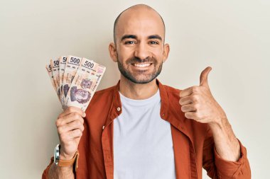 İspanyol asıllı genç adam 500 Meksika pezosu tutuyor mutlu ve olumlu gülümsüyor, başparmağıyla mükemmel ve onay işareti yapıyor. 