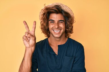 Yaz şapkası takan, gülümseyen ve kameraya göz kırpan genç İspanyol adam zafer işareti yapıyor. İki numara.. 
