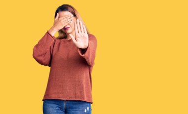 Güzel, genç bir kadın günlük kıyafetler ve gözlük takıyor. Gözleri ellerle örtüyor ve üzgün ve korku ifadeleriyle jest yapıyor. utangaç ve olumsuz kavram. 