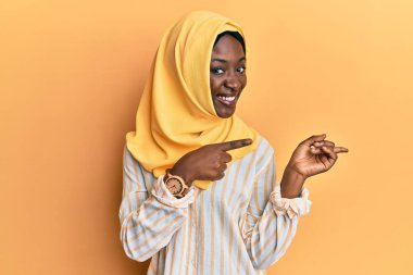 Güzel Afrikalı genç bir kadın geleneksel başörtüsü takıyor gülümsüyor ve kameraya bakıyor iki eliyle ve parmaklarıyla kenarı işaret ediyor.. 