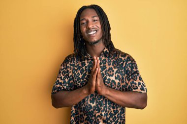 Saçları örgülü, leopar desenli hayvan desenli tişörtlü Afro-Amerikan bir adam. Elleriyle dua edip af diliyor.. 