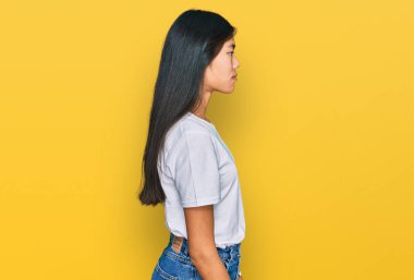 Güzel, beyaz tişört giyen Asyalı genç bir kadın. Yan tarafa bakıyor, rahat bir görünüm takınıyor. Doğal bir yüzü ve kendine güvenen bir gülümsemesi var.. 