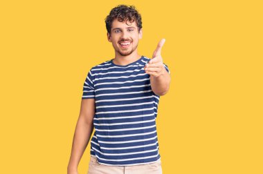 Kıvırcık saçlı, sıradan kıyafetler giyen, dostça gülümseyen ve selamlaşan genç, yakışıklı bir adam. başarılı iş. 