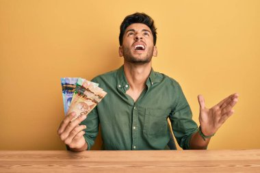 Genç yakışıklı adam Kanada doları tutuyor. Deli gibi bağırıyor ve bağırıyor. Saldırgan ifadeler ve kollar havada. hüsran kavramı. 