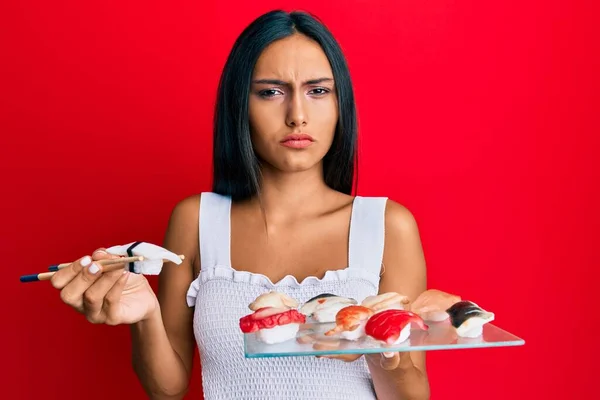 Молодая Брюнетка Женщина Ест Суши Баклажанов Используя Палочки Еды Скептически — стоковое фото
