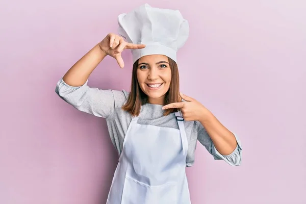 年轻美丽的女人穿着职业厨师的制服 戴着帽子 面带微笑 手指手画脚 面带笑容 创意与摄影概念 — 图库照片