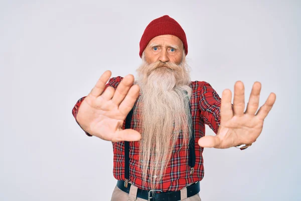 Old senior man with grey hair and long beard wearing hipster look with wool cap moving away hands palms showing refusal and denial with afraid and disgusting expression. stop and forbidden.