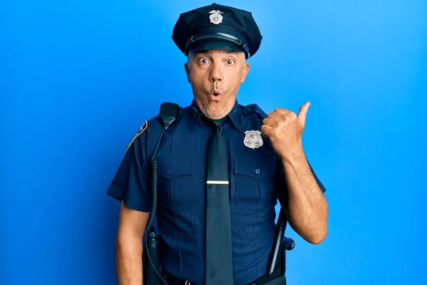 Handsome middle age mature man wearing police uniform surprised pointing with hand finger to the side, open mouth amazed expression.