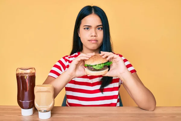 Fiatal Ázsiai Lány Eszik Egy Ízletes Klasszikus Burger Szkeptikus Ideges — Stock Fotó