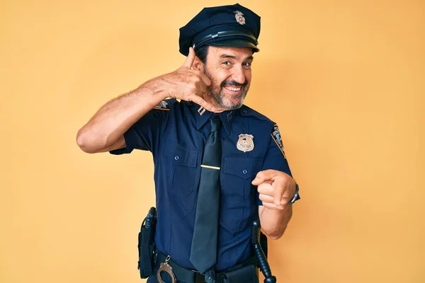 Middle age hispanic man wearing police uniform smiling doing talking on the telephone gesture and pointing to you. call me.