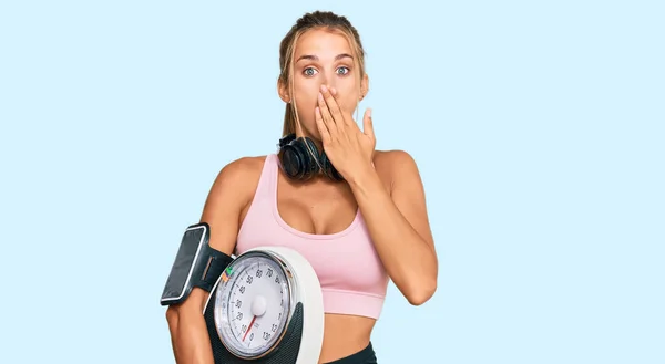 Young Blonde Woman Wearing Sportswear Holding Weighing Machine Covering Mouth — Stock Photo, Image