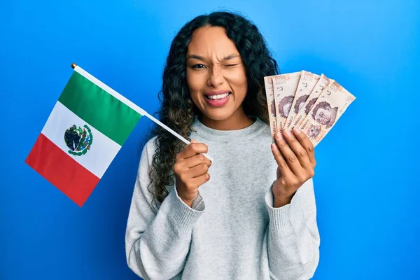 若いですラテン女性保持メキシコのフラグとメキシコのペソ紙幣ウインク見ますザカメラとともにセクシー表現 陽気で幸せな顔 — ストック写真