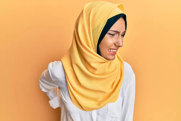 若いブルネットのアラブ女性は 伝統的なイスラムヒジャーブスカーフを身に着けています腰痛の苦しみ 手で背中に触れます 筋肉痛 — ストック写真