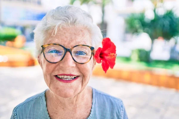 Yaşlı yaşlı, gri saçlı, dışarıda mutlu gülümseyen, dekoratif bir çiçek takan yaşlı kadın.