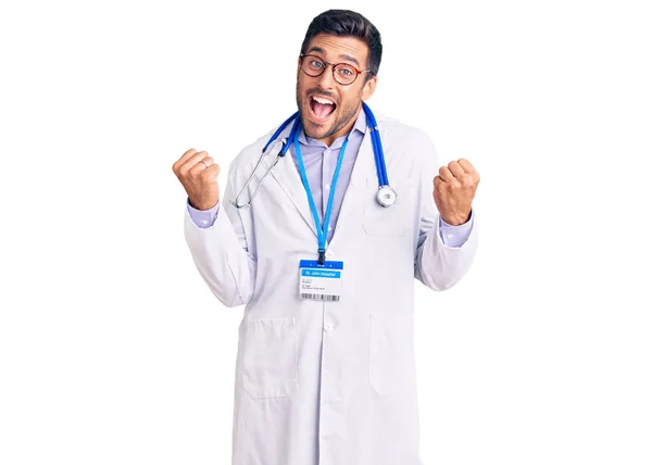医師の制服を着た若いヒスパニック系の男性と聴診器は非常に幸せと腕を上げて勝者のジェスチャーを行う興奮 笑顔と成功のために叫んで お祝いのコンセプト — ストック写真