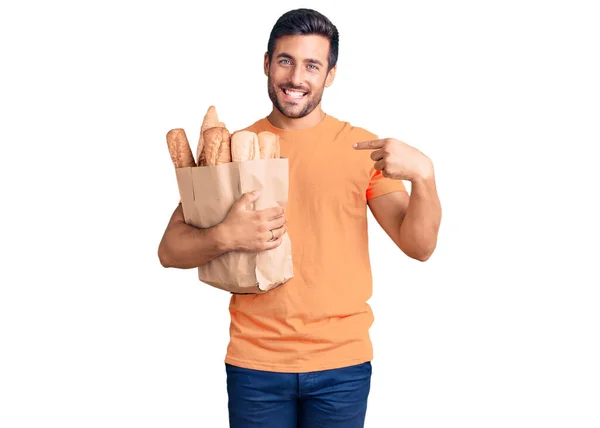 Junger Hispanischer Mann Hält Papiertüte Mit Brot Und Zeigt Mit — Stockfoto