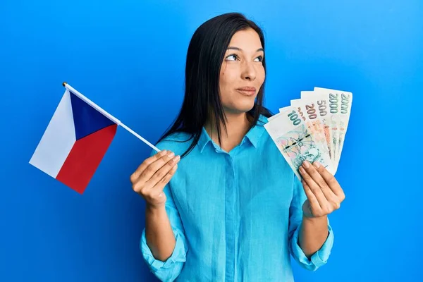 年轻的拉丁女子拿着切赫共和国国旗和科鲁纳钞票 面带微笑地看着旁边 目不转睛地看着外面想 — 图库照片