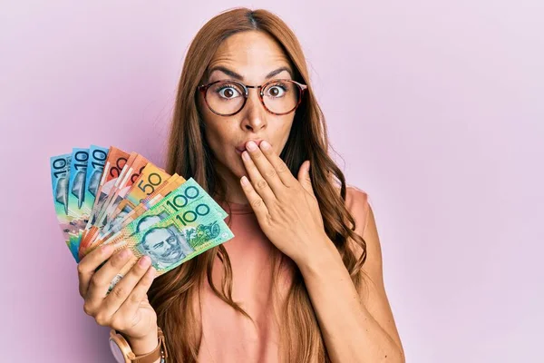 Młoda Brunetka Trzymająca Australijskie Dolary Zakrywające Usta Ręką Zszokowana Przerażona — Zdjęcie stockowe