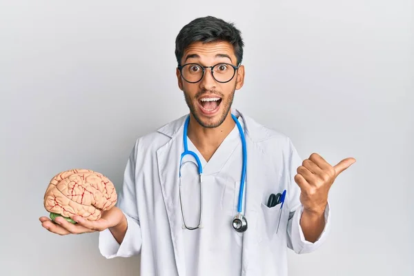 Jovem Bonito Homem Vestindo Médico Casaco Segurando Cérebro Apontando Polegar — Fotografia de Stock